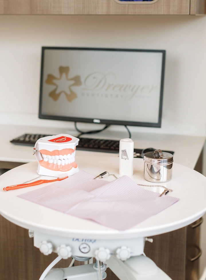 Dental office treatment table displays educational teeth model, orange toothbrush, and dental instruments.