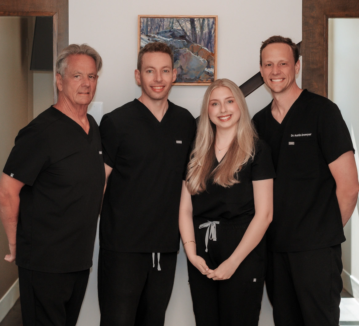 Four dental professionals in black scrubs standing together in a modern dental office setting.